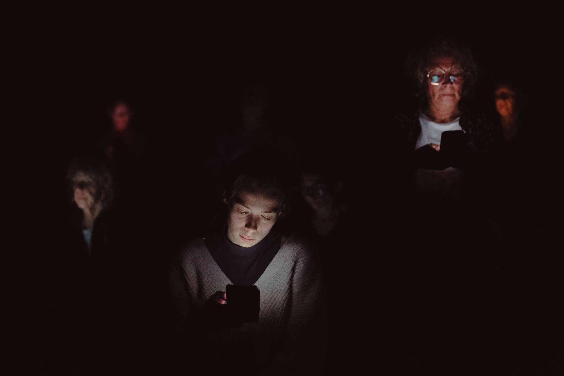Dans la pénombre, trois visages apparaissent grâce à la lumière du portable tenu dans les mains des interprètes. 