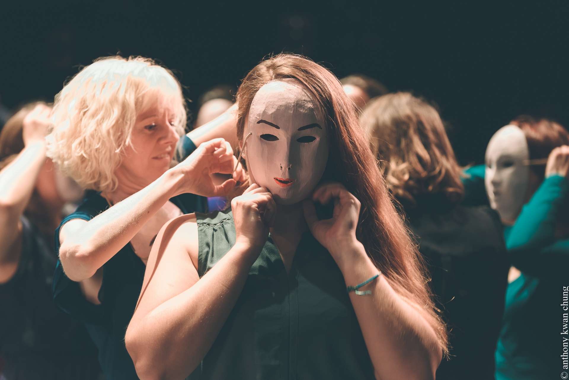 Portrait d'une femme masquée qui se fait attacher son masque par une autre femme. 