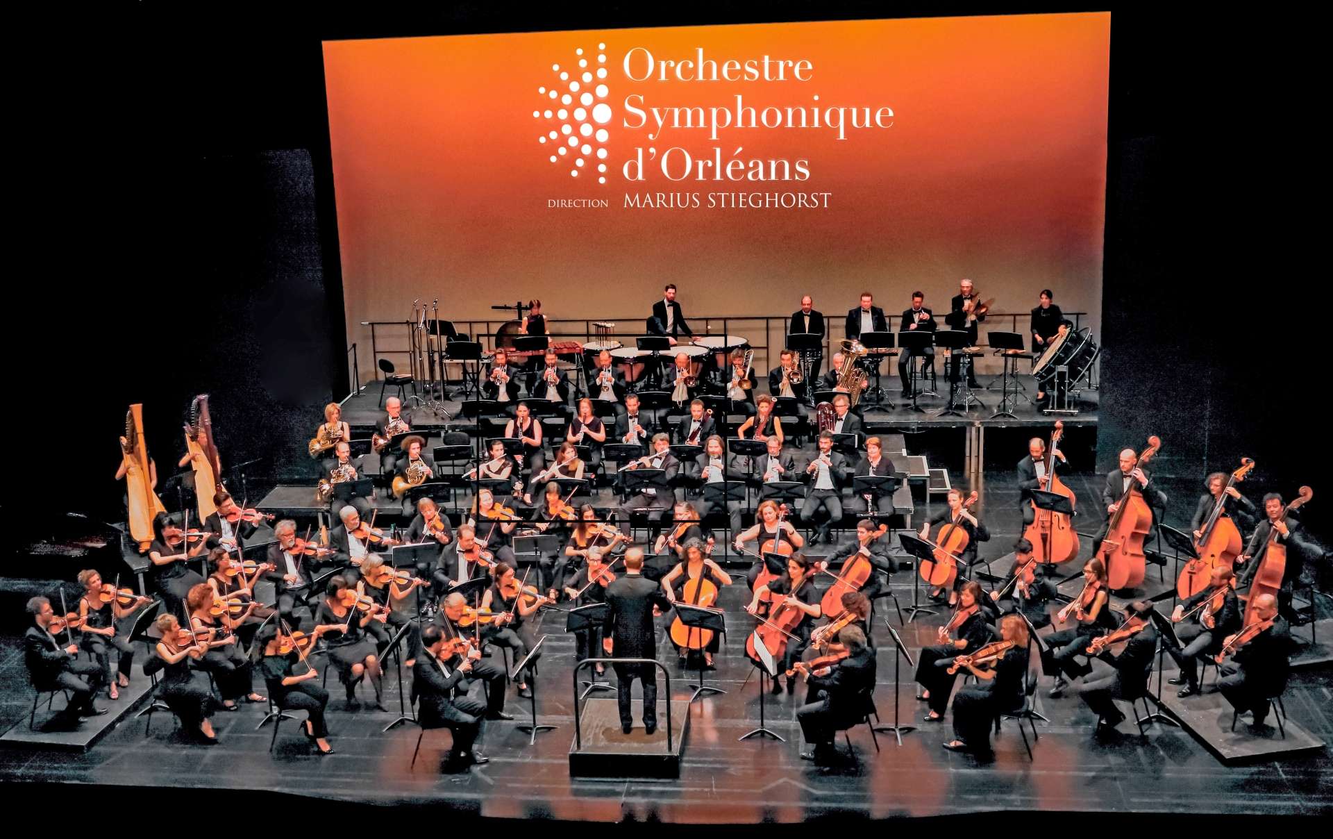 Les musiciens et musiciennes de l'Orchestre Symphonique d'Orléans sur scène face à leur chef d'orchestre. 
